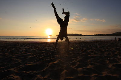 Silhouette of person standing on beach at sunset