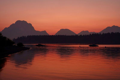 Scenic view of lake by silhouette mountains against sky during sunset