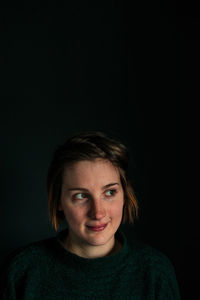 Portrait of young woman against black background