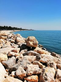 Rocks by sea against clear blue sky