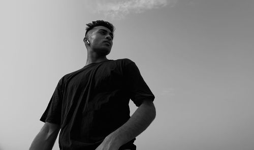 Low angle view of young man looking away against sky