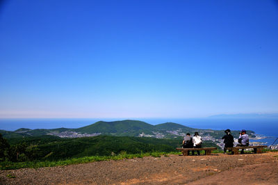 People sitting on mountain against clear blue sky