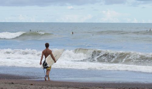 Rear view of man walking on beach against sky