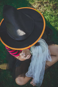 High angle view of woman wearing witch hat holding human skull while sitting on field in park