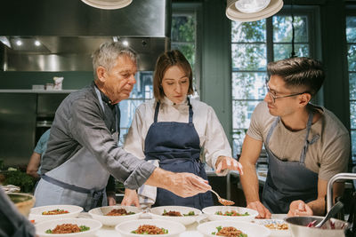 Female chef teaching male students during cooking class in kitchen