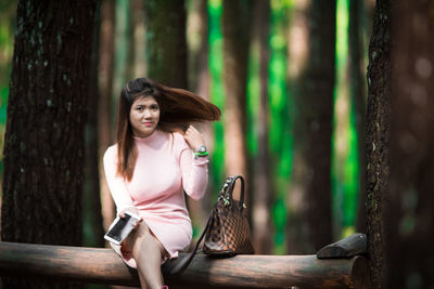 Portrait of beautiful woman sitting on fallen tree at forest