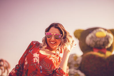 Portrait of smiling young woman wearing sunglasses against sky