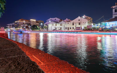 Illuminated buildings by lake against sky in city at night