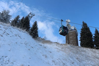 Low angle view of ski lift over snow covered mountains against sky