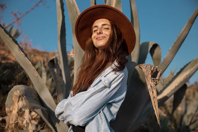 Smiling young woman wearing a hat at an agave in the countyside