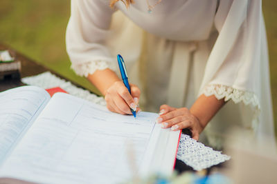 Midsection of woman writing in book on table