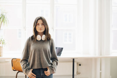 Portrait of young woman standing against wall