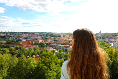 Rear view of woman looking at cityscape against sky