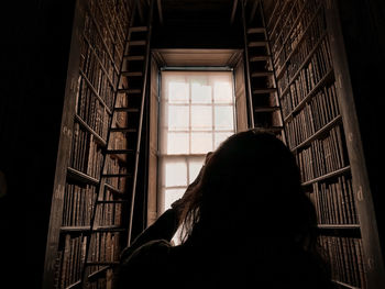 Rear view of woman looking through window library