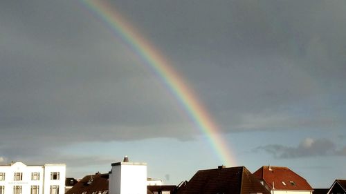 Low angle view of rainbow over houses against sky