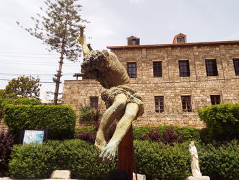 Low angle view of statue by building against sky