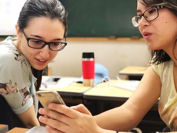 Woman showing mobile phone to friend in classroom