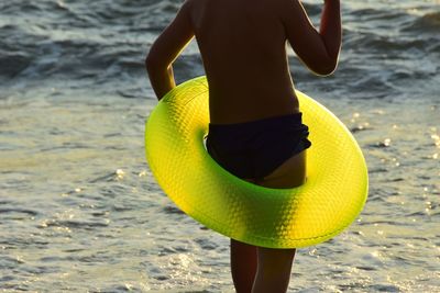 Midsection of man with inflatable ring standing at beach