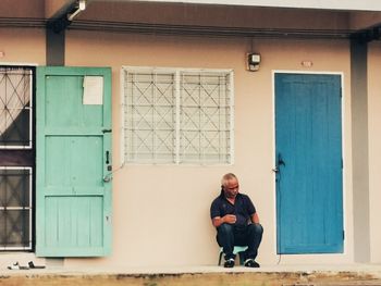 Full length portrait of young man sitting by door