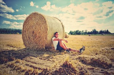 Full length of man sitting by hay bale on field