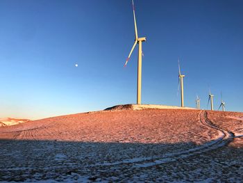 Wind turbines on land against clear sky