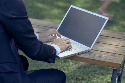 Midsection of man using mobile phone while sitting on bench