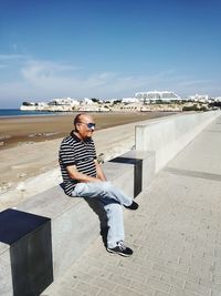 Full length of man sitting on shore against sky