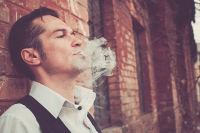 Man smoking will standing against wall