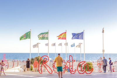 Rear view of people standing at beach against clear sky