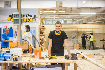 Portrait of confident young trainee standing at workbench at illuminated workplace