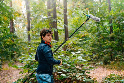 Side view of man with boom microphone standing in forest
