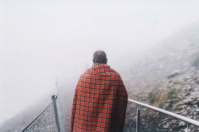 Rear view of man standing on railing against mountain