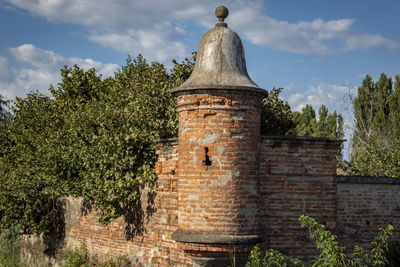 Old stone wall by trees and building against sky