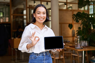 Portrait of smiling young woman using digital tablet in cafe