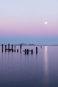 Silhouette wooden posts in calm sea at sunset