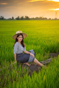 Portrait of woman sitting on field against sky during sunset
