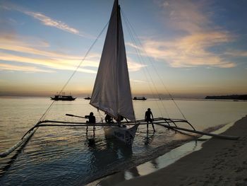 Silhouette people on sailboat by sea against sky during sunset