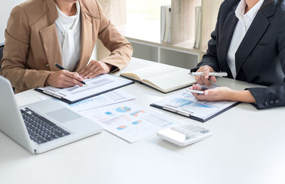 Midsection of businesswomen at desk using laptop and mobile phone
