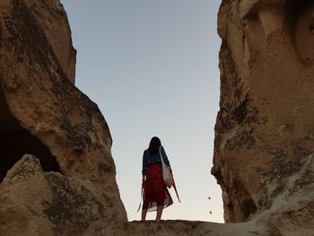 Rear view of woman walking on rocks against clear sky