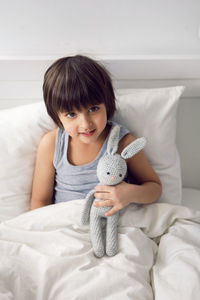 Child boy lies in a white children's bed with a blanket in a room with toys rabbits hug