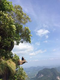 Side view of man sitting on rock at mountain against sky