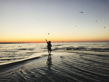 Silhouette woman standing on beach against sky during sunset