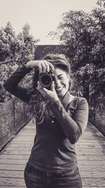 Portrait of woman photographing by tree