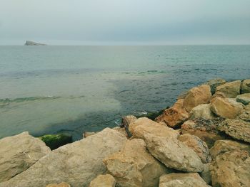 Scenic view of rocks by sea against sky