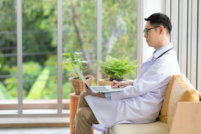 Midsection of man using mobile phone while sitting on window