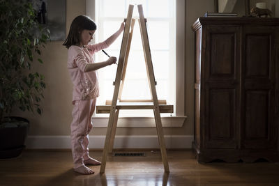 Side view of girl drawing on artist's canvas while standing at home