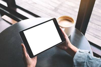 Cropped hand of woman holding digital tablet sitting at cafe