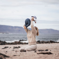 Side view of woman exercising at beach against sky