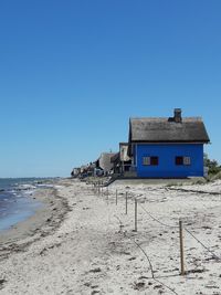 House on beach by building against clear blue sky