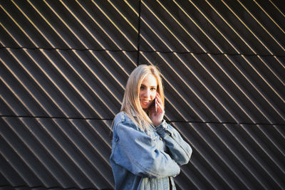 Portrait of young woman talking on mobile phone against wall